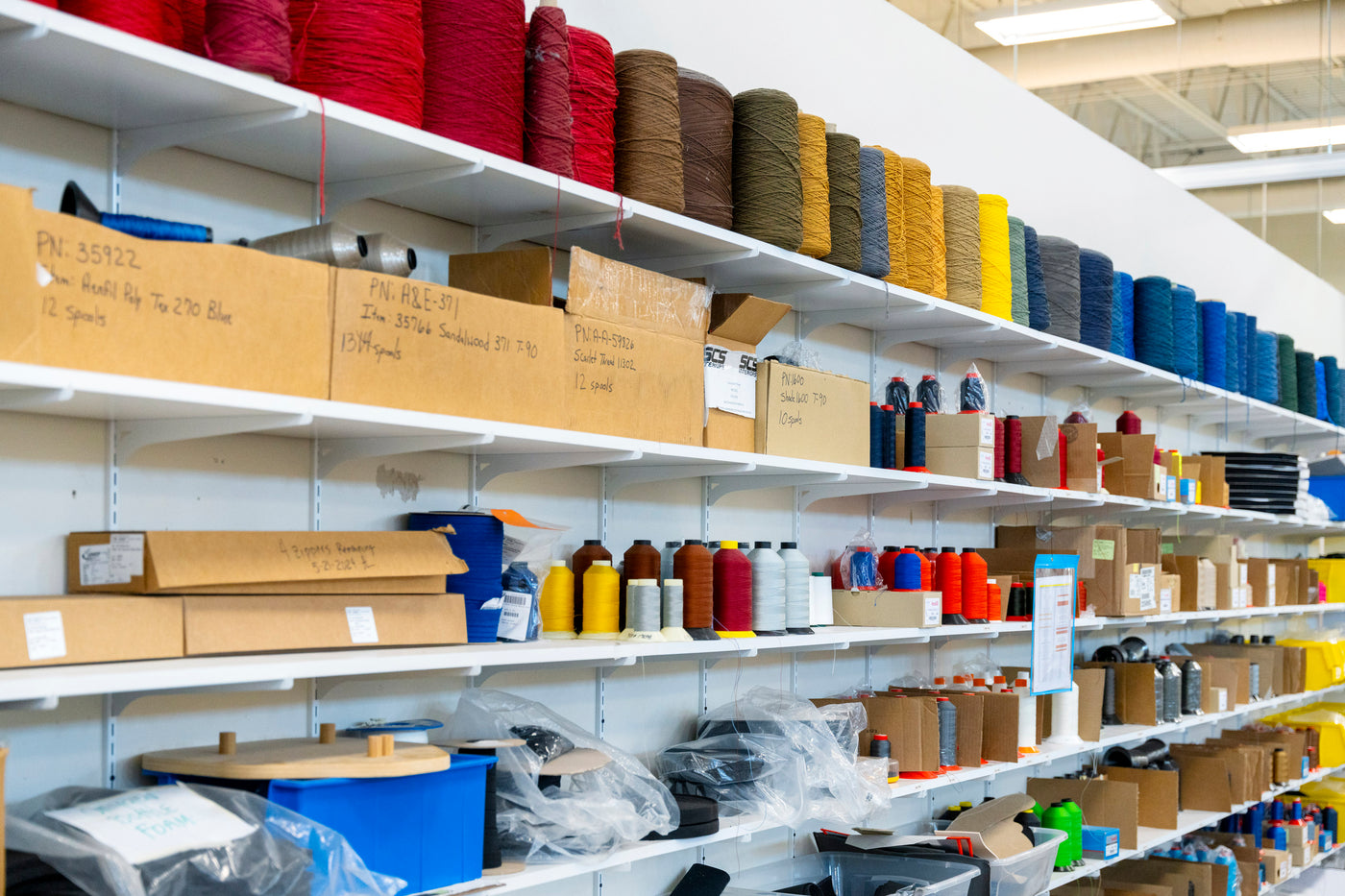 Shelves stocked with various colored spools of thread and boxes in a warehouse setting.